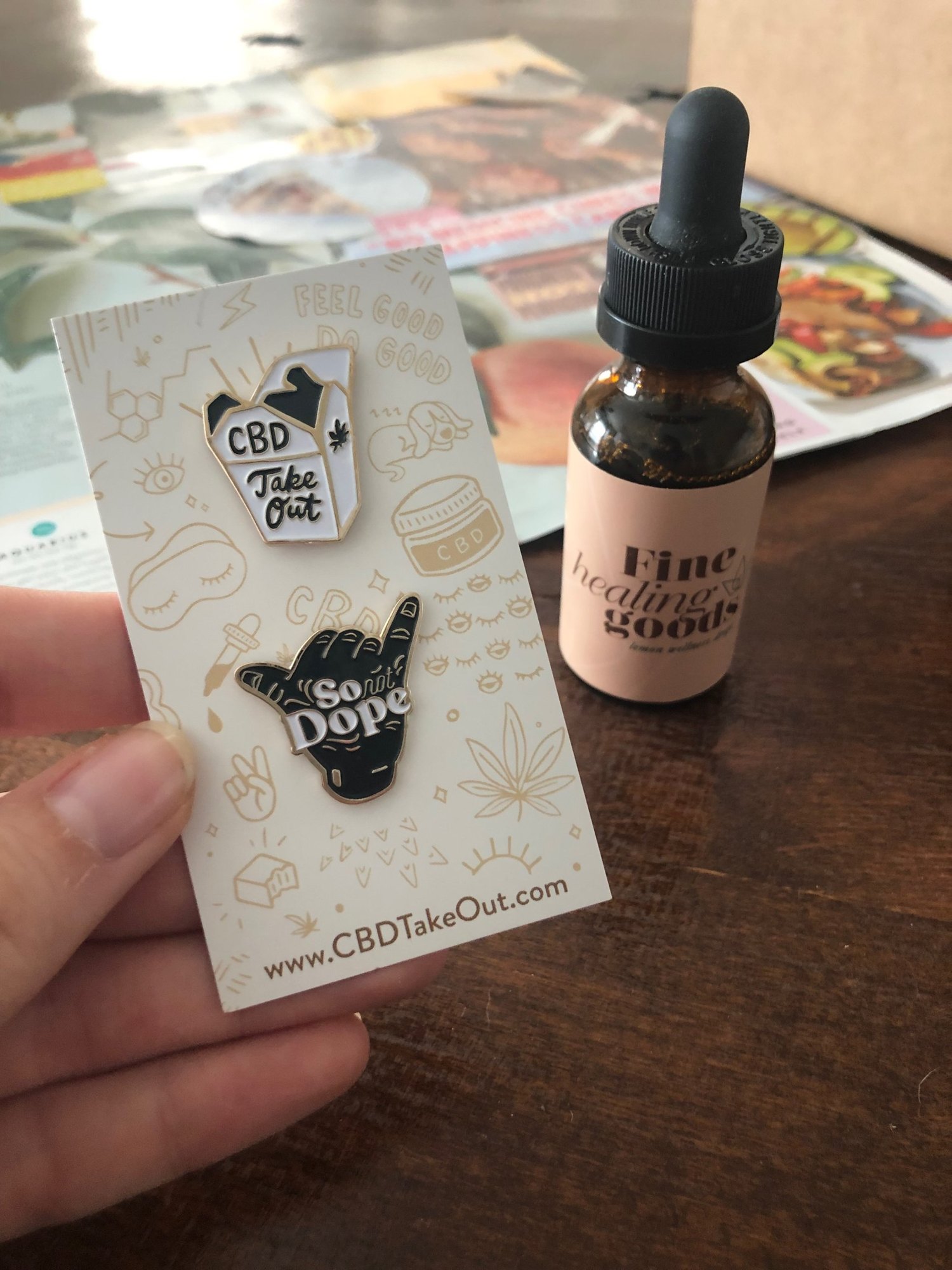 CBD Takeout enamel pins, a takeout box and a So Not Dope hand, on a cream backing card printed with the gold line illustration pattern