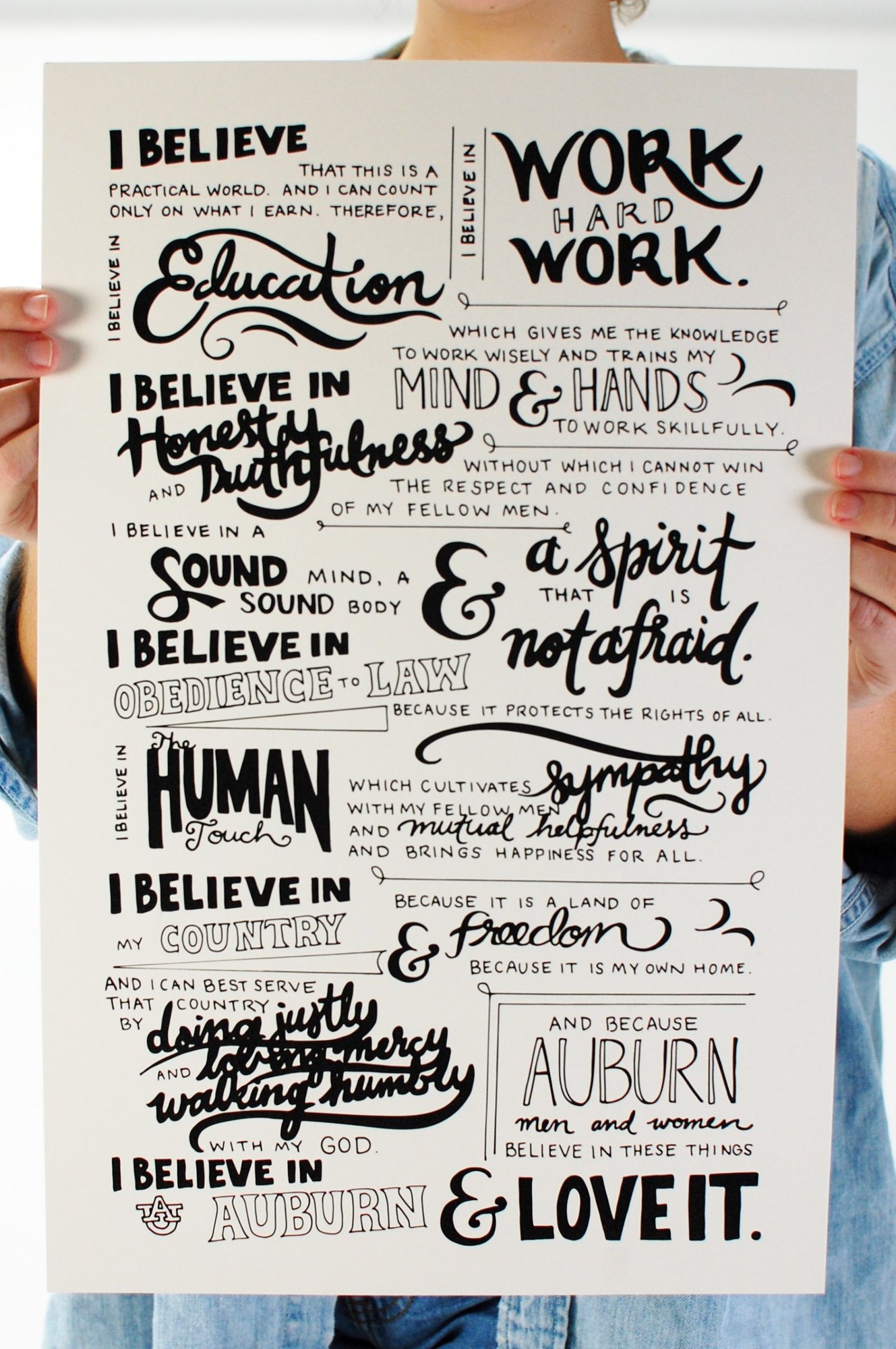 A printed poster of the Auburn Creed, fully hand-lettered in many styles, held up by the designer